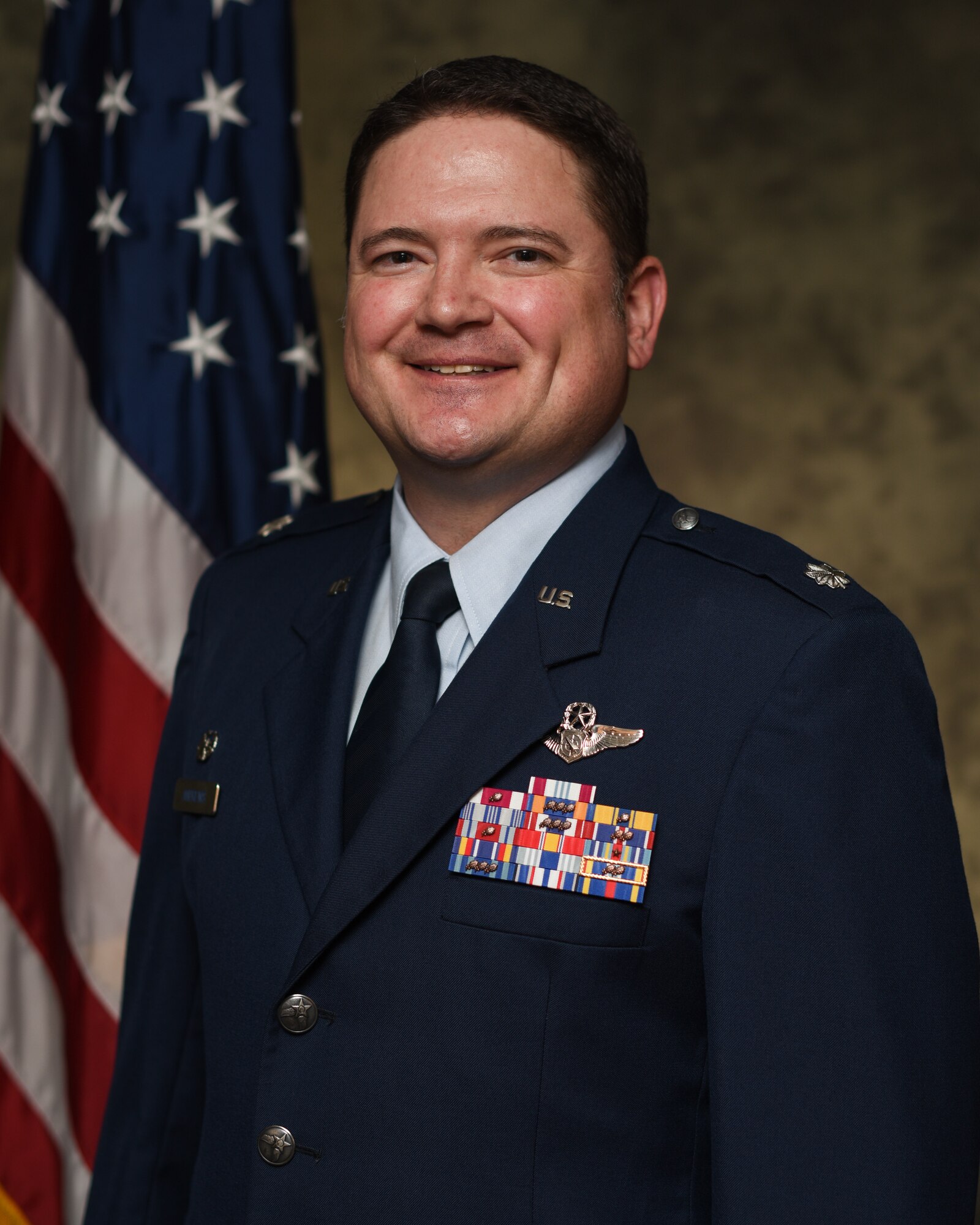 photo of uniformed U.S. Air Force Airman standing in front of a U.S. flag