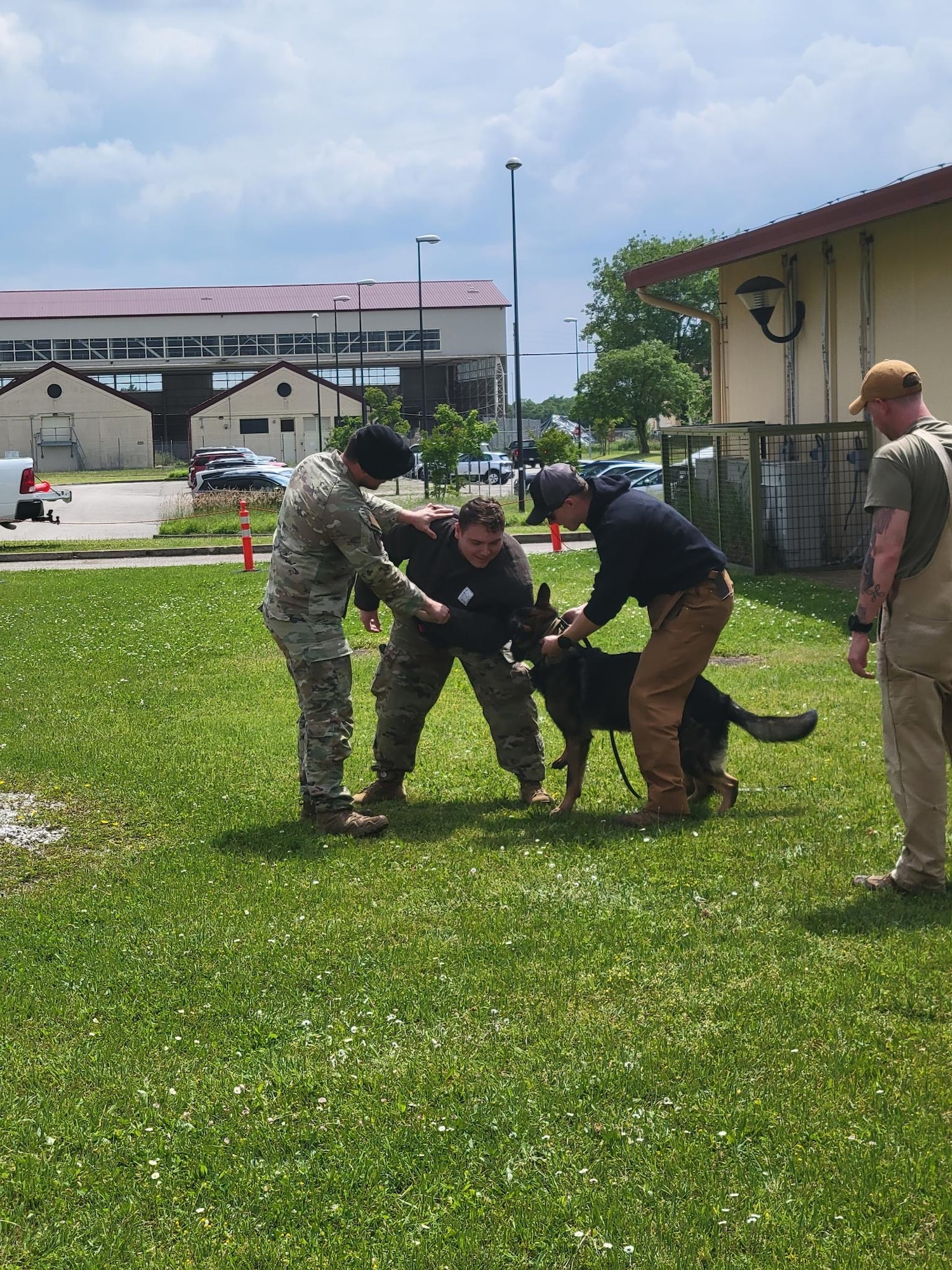 A man in a safety suit is attacked by a police K-9 as the dog's handlers observe and facilitate the demonstration.