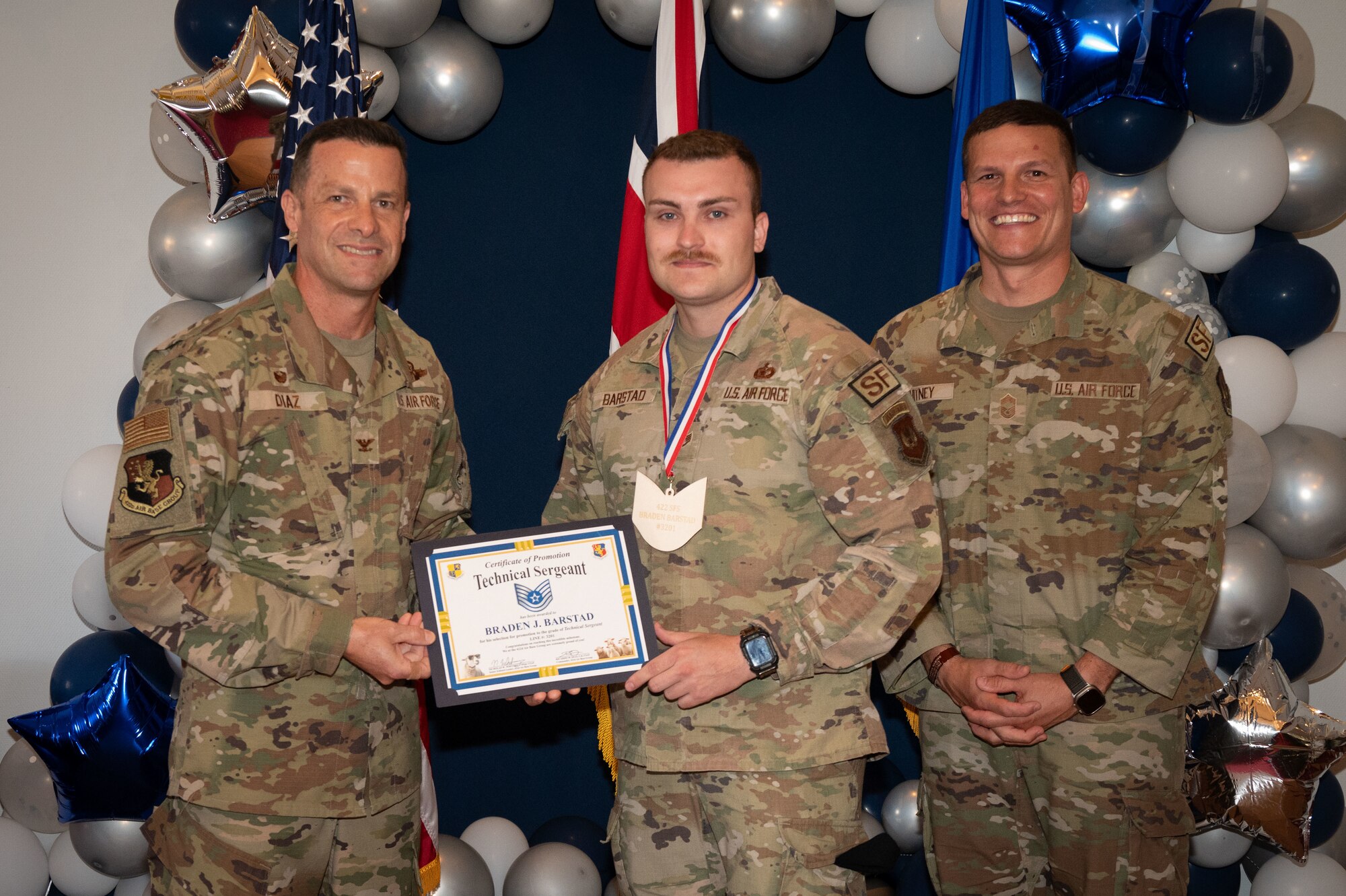 U.S. Air Force Col. Ricardo M. Diaz, left, 422nd Air Base Group commander, and Chief Master Sgt. Nicholas Whitney, right, 422nd Air Base Group senior enlisted leader, present a certificate of promotion to Staff Sgt. Braden J. Barstad, assigned to 422nd Security Forces Squadron.