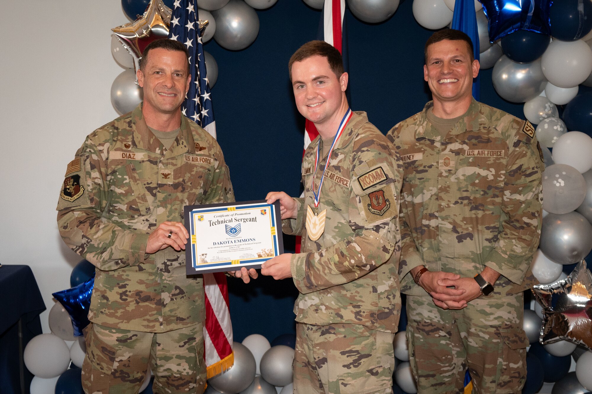 U.S. Air Force Col. Ricardo M. Diaz, left, 422nd Air Base Group commander, and Chief Master Sgt. Nicholas Whitney, right, 422nd Air Base Group senior enlisted leader, present a certificate of promotion to Staff Sgt. Dakota Emmons assigned to the 422nd Communications Squadron.