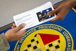 A travel assistant passes a debit card to an enlistee. USMEPCOM replaced meal checks for enlistees traveling to initial entry training with debit cards starting June 28, 2024.