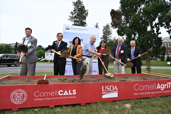 Seven people posing throwing shovels of dirt in the air during a groundbreaking ceremony.