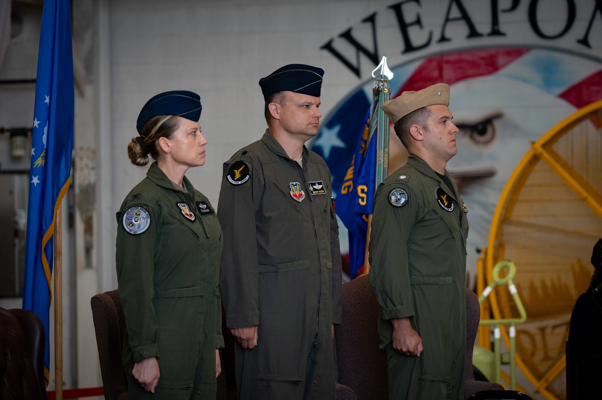 U.S. Air Force Col. Candice Sperry, 350th Spectrum Warfare Group commander, left, U.S. Air Force Lt. Col. Darren Woodside, 513th Electronic Warfare Squadron commander, center, and U.S. Navy Cmdr. Alexander Sandroni, 513th EWS deputy commander, right, stand at attention during the 513th EWS change of command ceremony at Eglin Air Force Base, Florida, June 18, 2024. The 513th is responsible for providing mission data file reprogramming support to all United States F-35s. (Courtesy Photo)