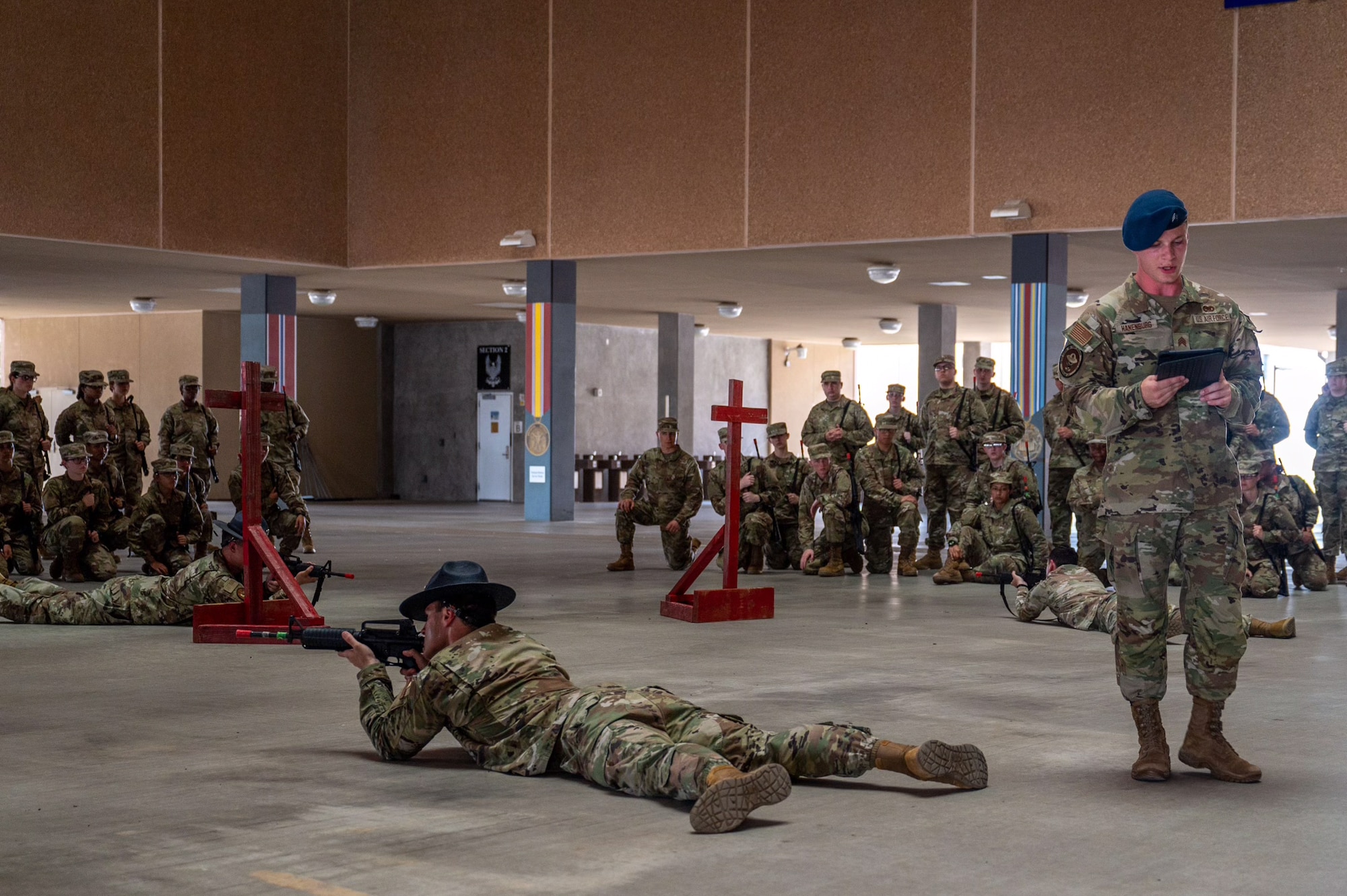 U.S. Air Force Academy Cadet 2nd Class Seth Hanenburg (standing) presents a weapons handling lesson to Basic Military Training trainees with the 321st Training Squadron while Military Training Instructors demonstrate how to use the weapons on June 17, 2024, at Joint Base San Antonio-Lackland, Texas. The Summer Leadership Program at USAFA provides cadets with the opportunity to collaborate with BMT MTIs at the 737th Training Group for three weeks in June. When cadets return to USAFA in the fall, they will lead the six-week indoctrination program, Basic Cadet Training, for incoming USAFA students. The 321 TRS, is just one of 10 training squadrons, that guide and coach the next generation of Airmen at BMT. (U.S. Air Force photo by Ava Leone)