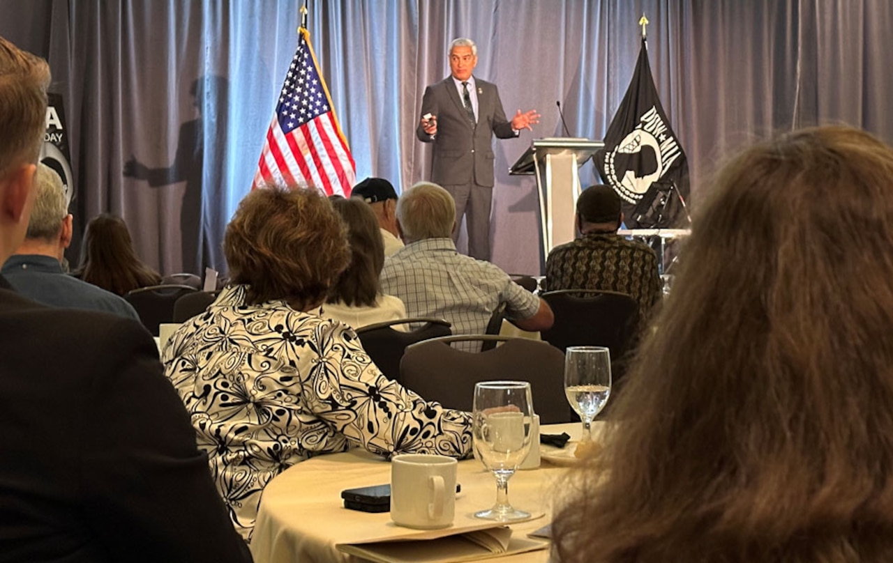 A man speaks to a group of military and civilian personnel.