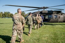 Members of Joint Task Force-National Capital Region walk in a line toward a helicopter, which is parked on green grass