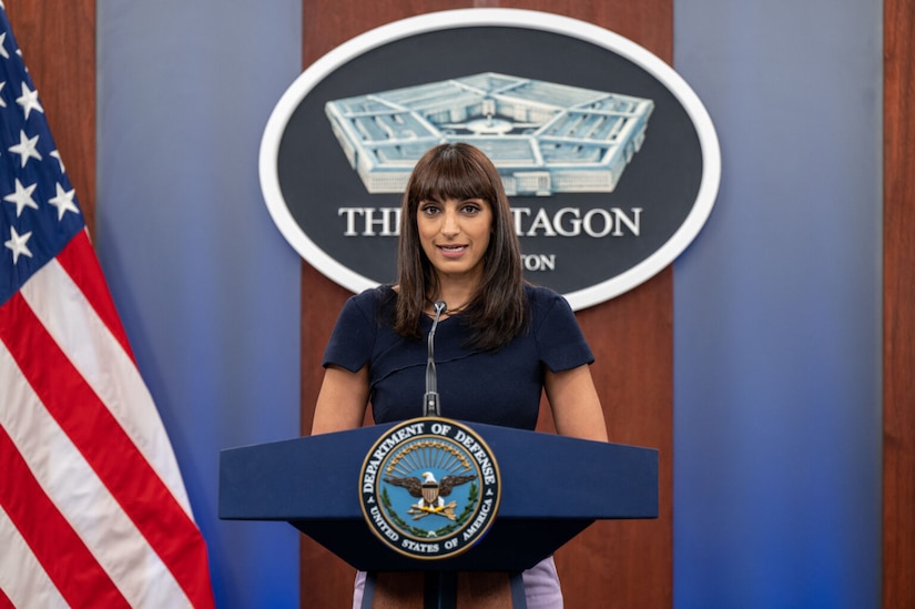 A woman stands behind a podium and speaks into a microphone.