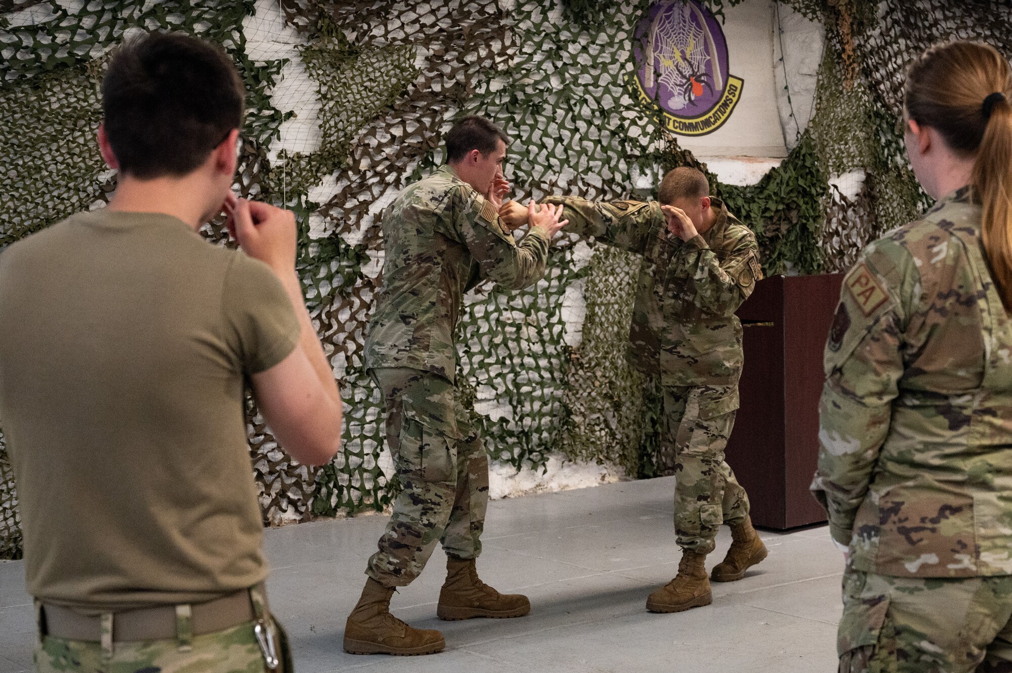 U.S. Air National Guard Airmen practice combative maneuvers inside a gym. The Airmen are wearing OCP pattern uniforms.
