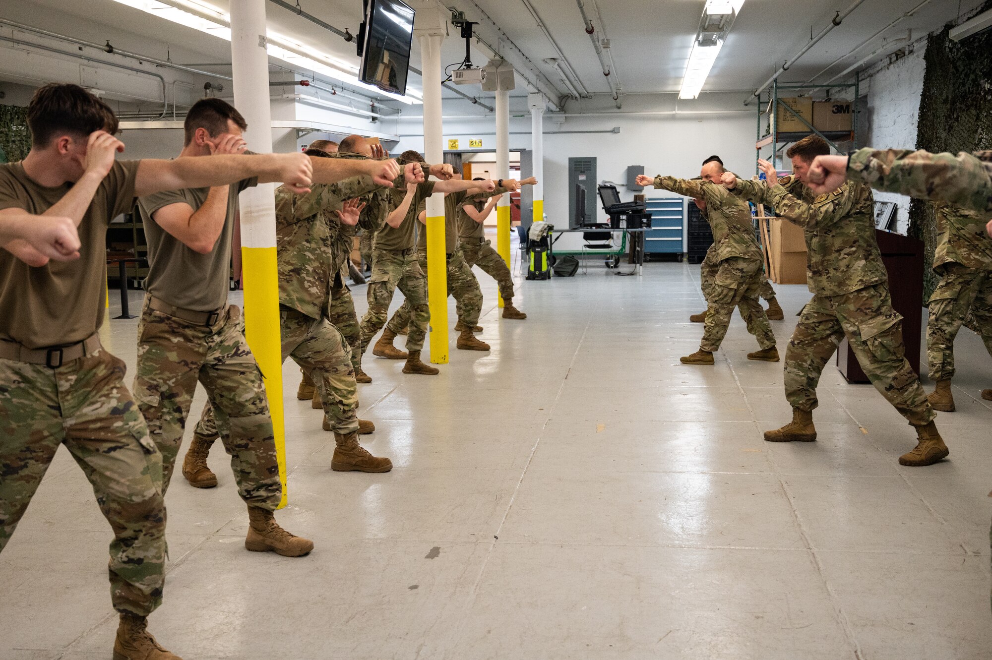 U.S. Air National Guard Airmen practice combative maneuvers inside a gym. The Airmen are wearing OCP pattern uniforms.