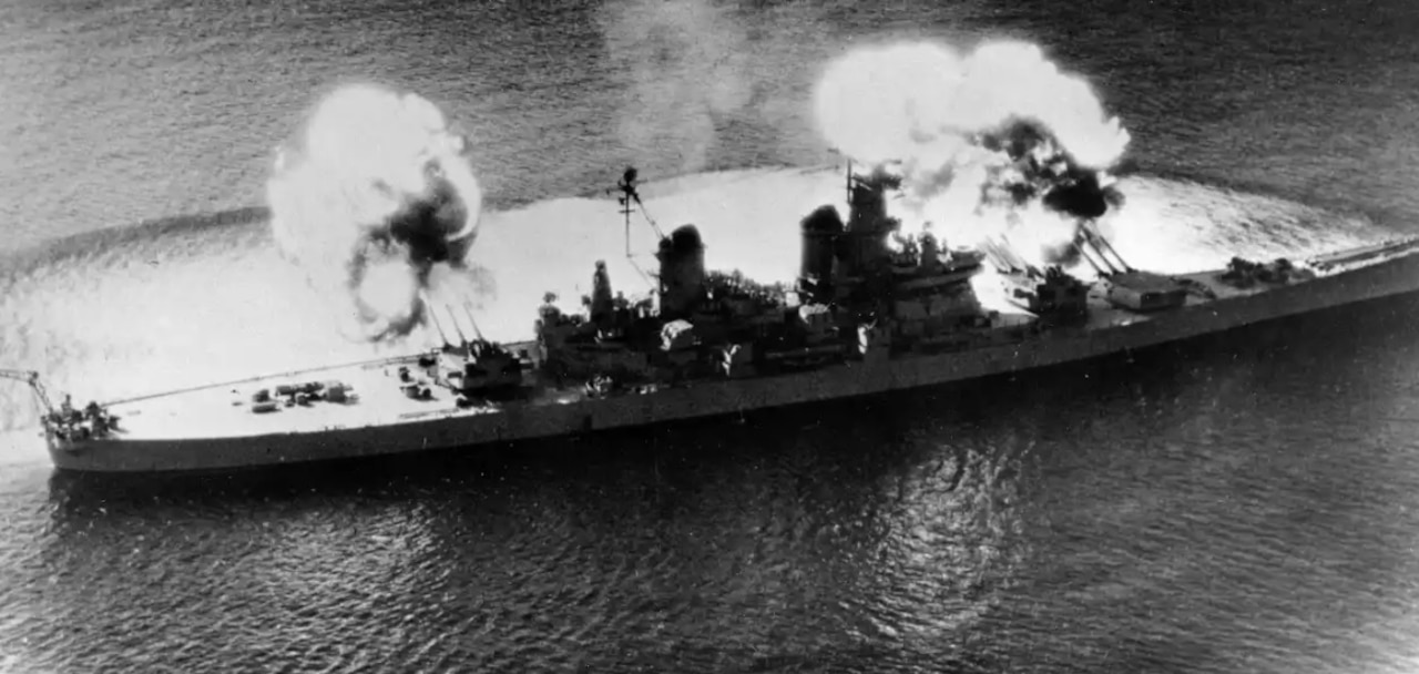 In a black and white image, weapons are fired from a military ship at sea.