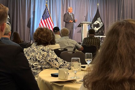 A man speaks to a group of military and civilian personnel.