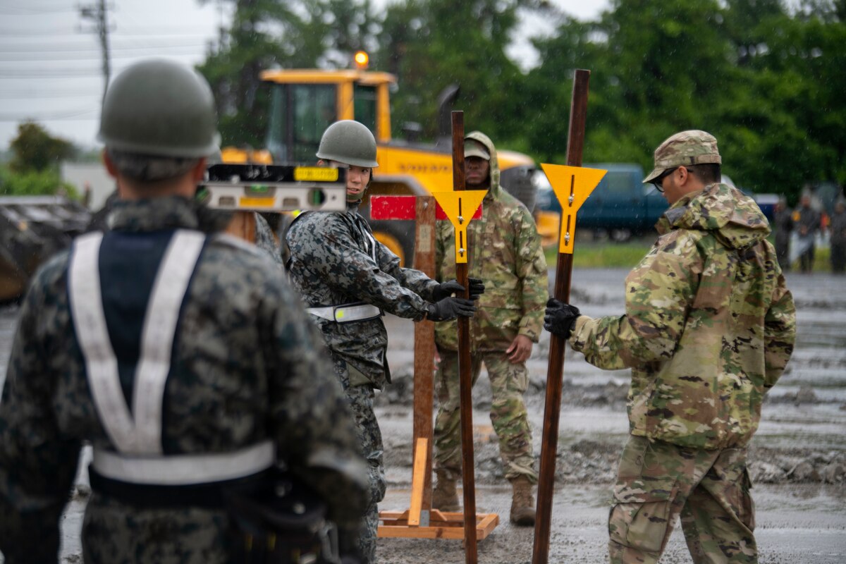 Two Japan Air Self-Defense Force members and two U.S. Air Force members use wooden posts with yellow triangles to mark the cement.