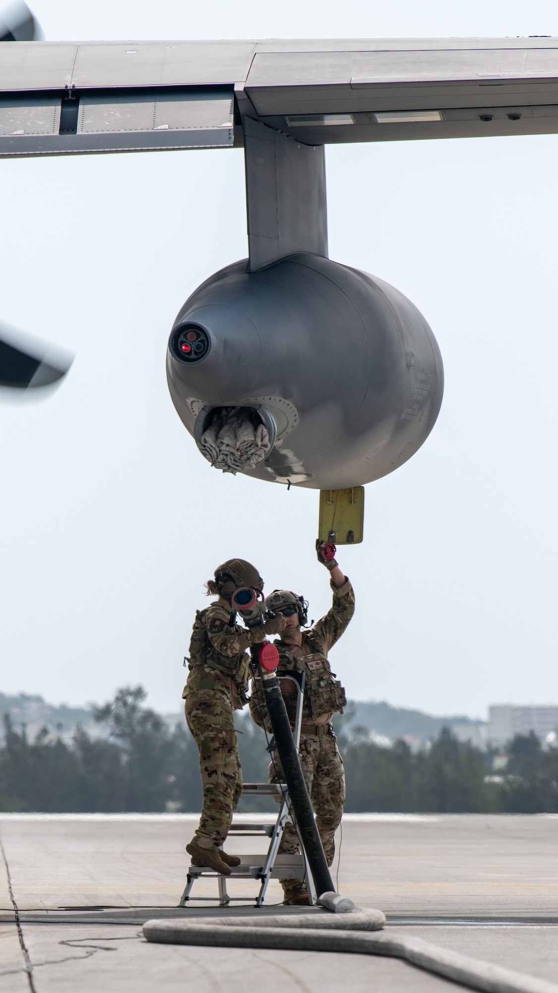 Two Airmen connect a hose to a fuel container of a transport plane.