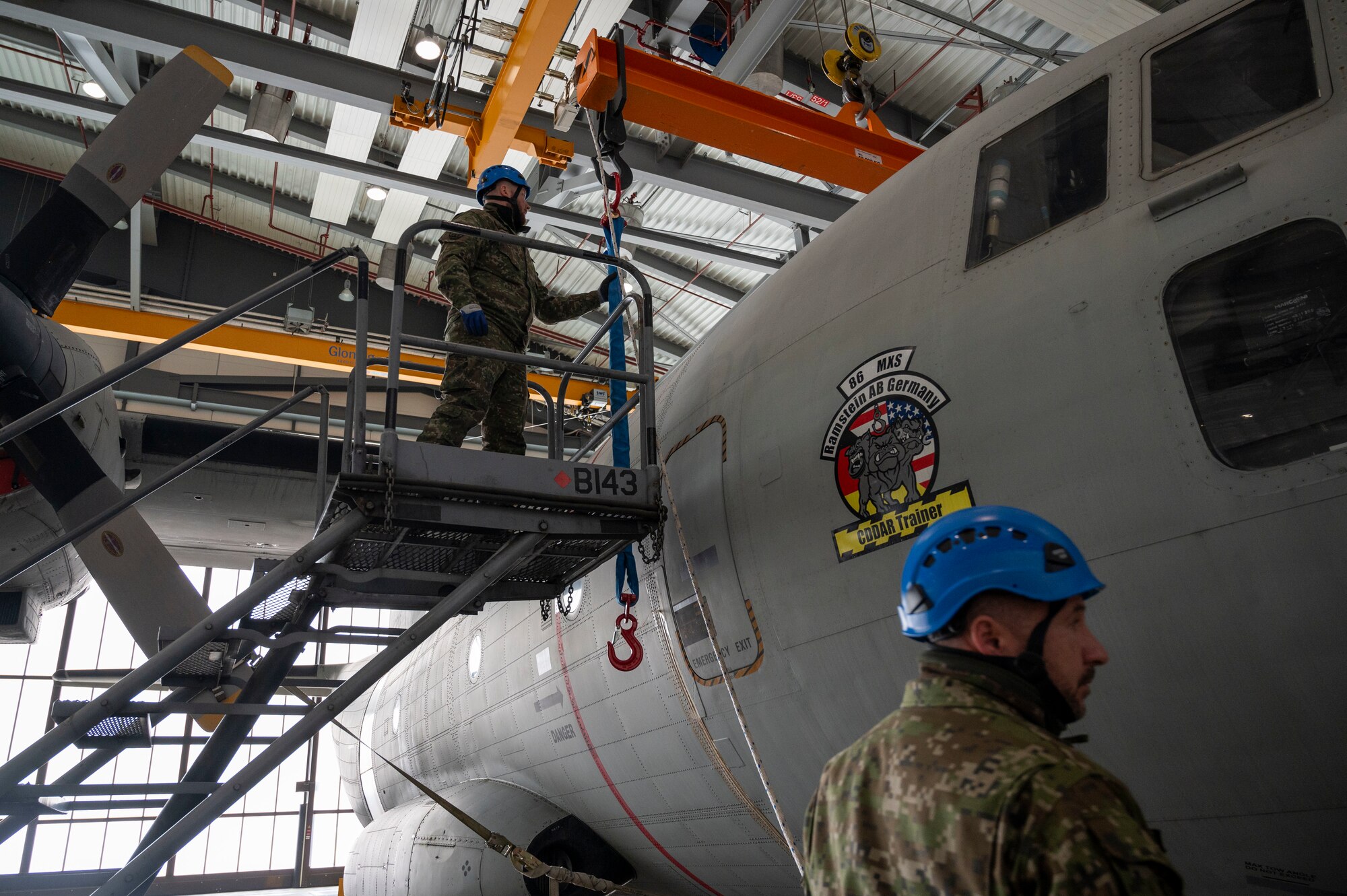 A man stands on a ladder next to a plane while adjusting a crane over it.