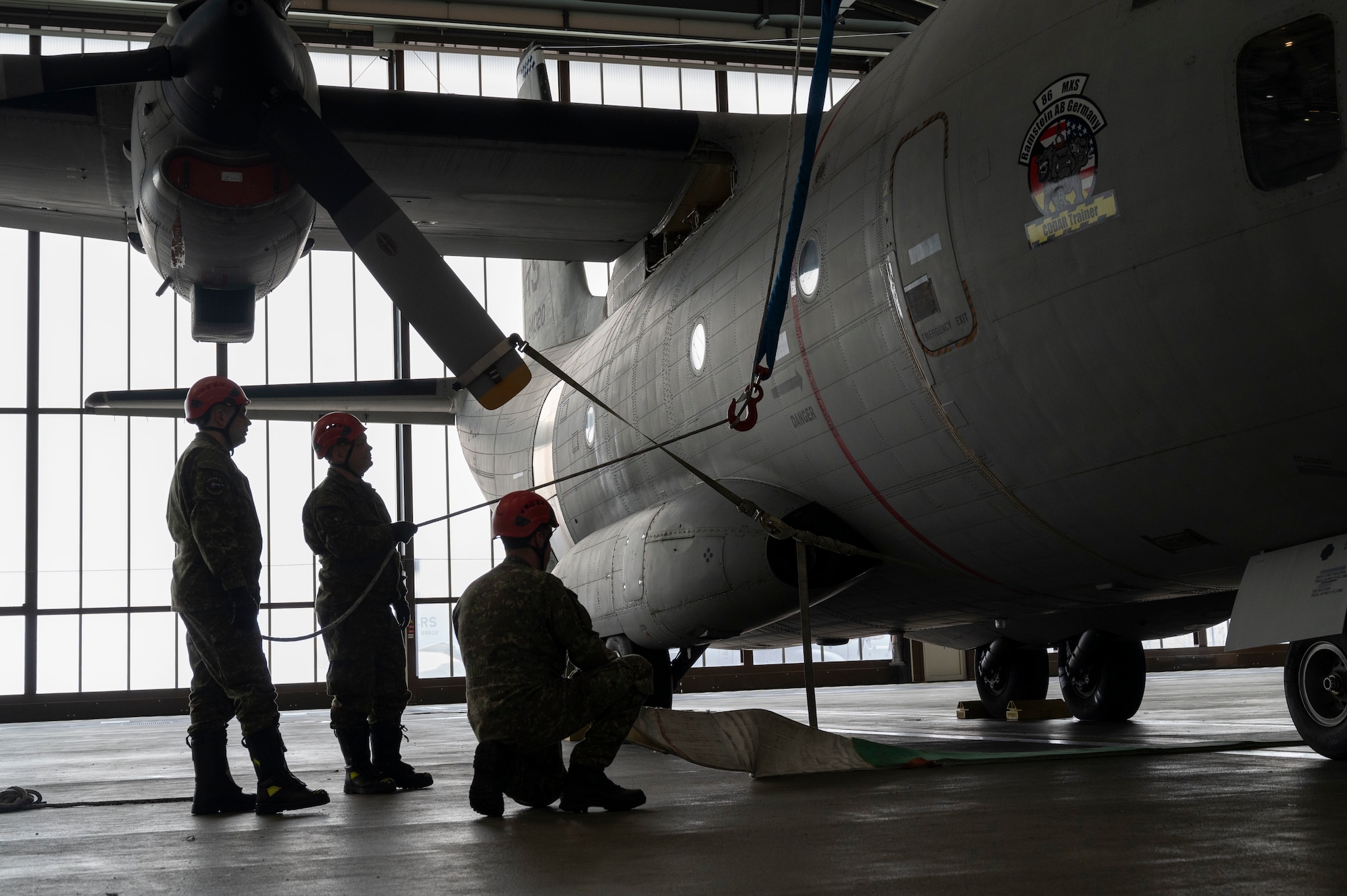 Three men adjust a strap attached to a crane over an aircraft