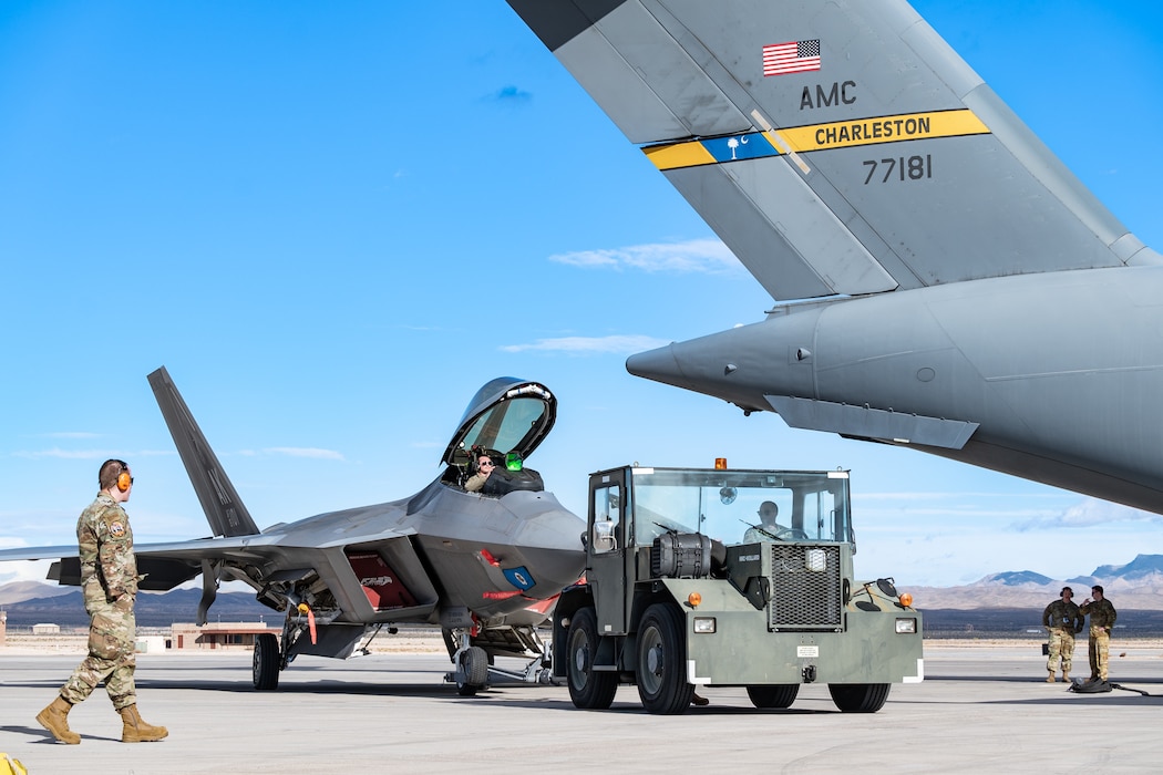 An MB4 tow tractor pulls an F-22 Raptor to be refueled by a C-17 Globemaster III