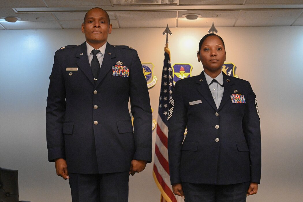 A man and woman in uniform stand at attention.