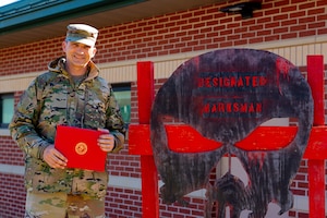 Airman stands beside a sign.