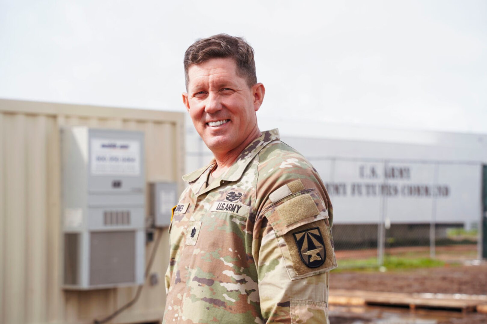 A service member stands in front of a trailer while posing for a photo.