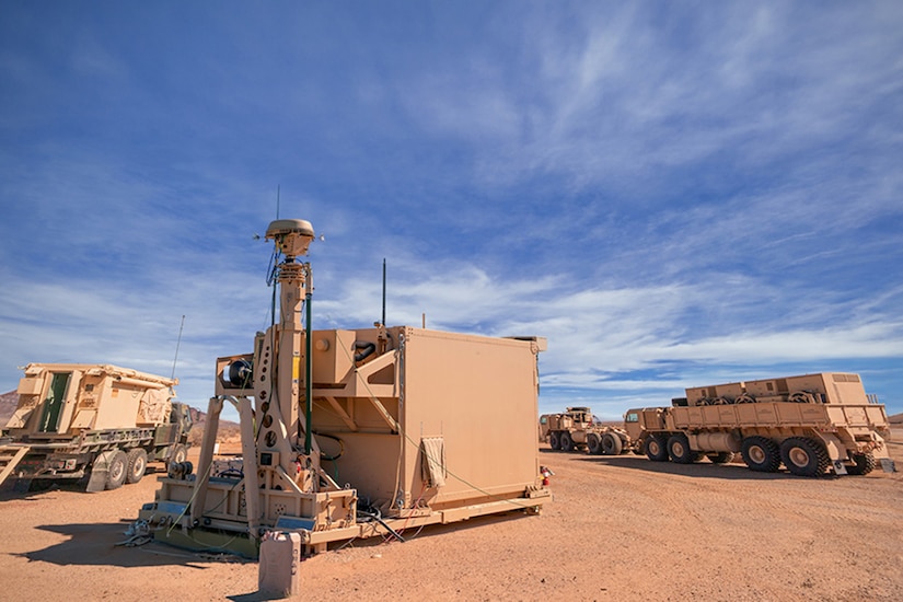 An integrated battle command system equipment sits on the desert in front of military vehicles.