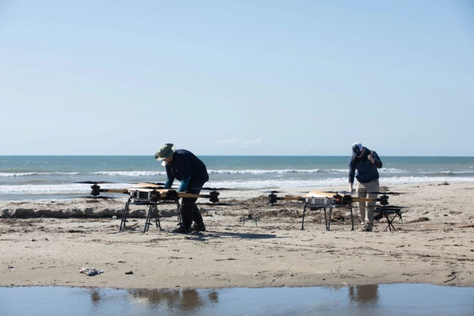 Two civilians adjust two small, unmanned aircraft.
