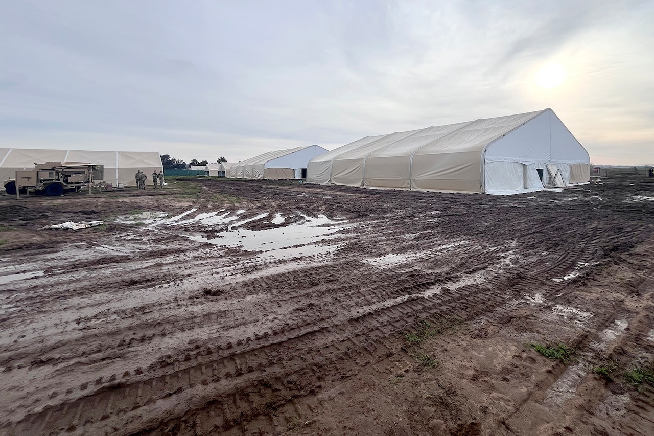 Military tents in a muddy field are shown.