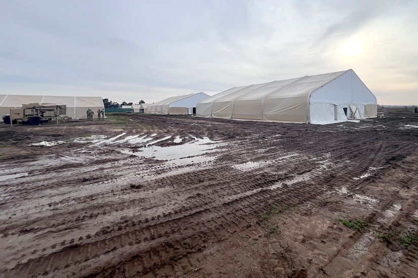 Military tents in a muddy field are shown.