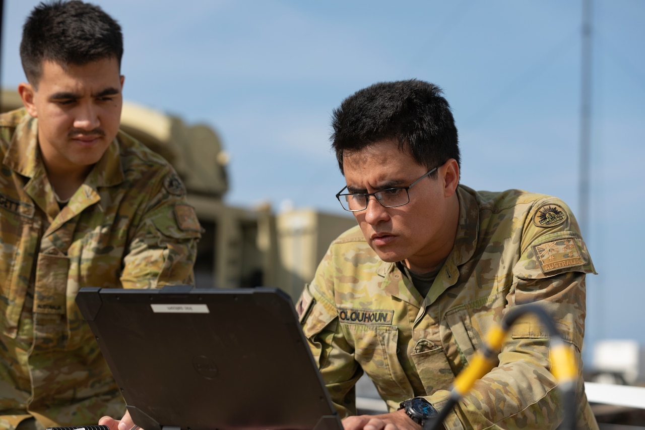 Two men in uniforms look at laptop screen.