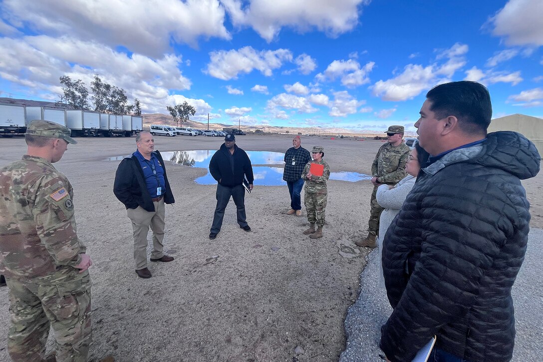 Military members and civilians meet outside of a warehouse.