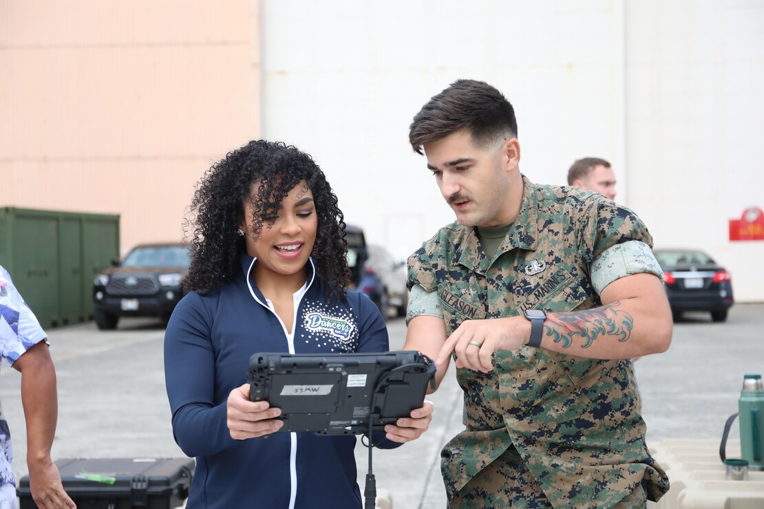 U.S. Marine Corps Sgt. Shawn Gleason, explosive ordnance disposal technician, Marine Wing Support Squadron 174, Marine Aircraft Group 24, 1st Marine Aircraft Wing, instructs NFL cheerleader, Geena Rojas, during the Armed Forces Entertainment’s Pro Blitz Tour 2024 at Marine Corps Base Hawaii, Feb. 2, 2024. The visit provided service members and their families the opportunity to meet retired and current NFL cheerleaders and Football Hall of Fame Honorees. (U.S. Marine Corps photo by Lance Cpl. Samuel Estridge)