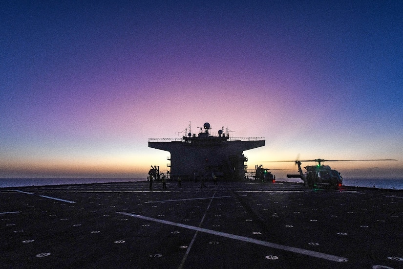 A ship's deck is in view with two helicopters at the far end with a dark violet backdrop.