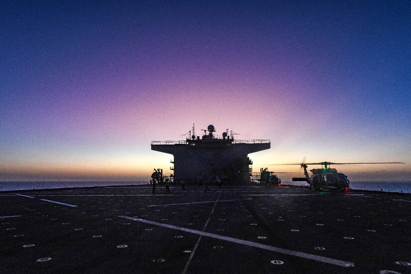 A ship's deck is in view with two helicopters at the far end with a dark violet backdrop.