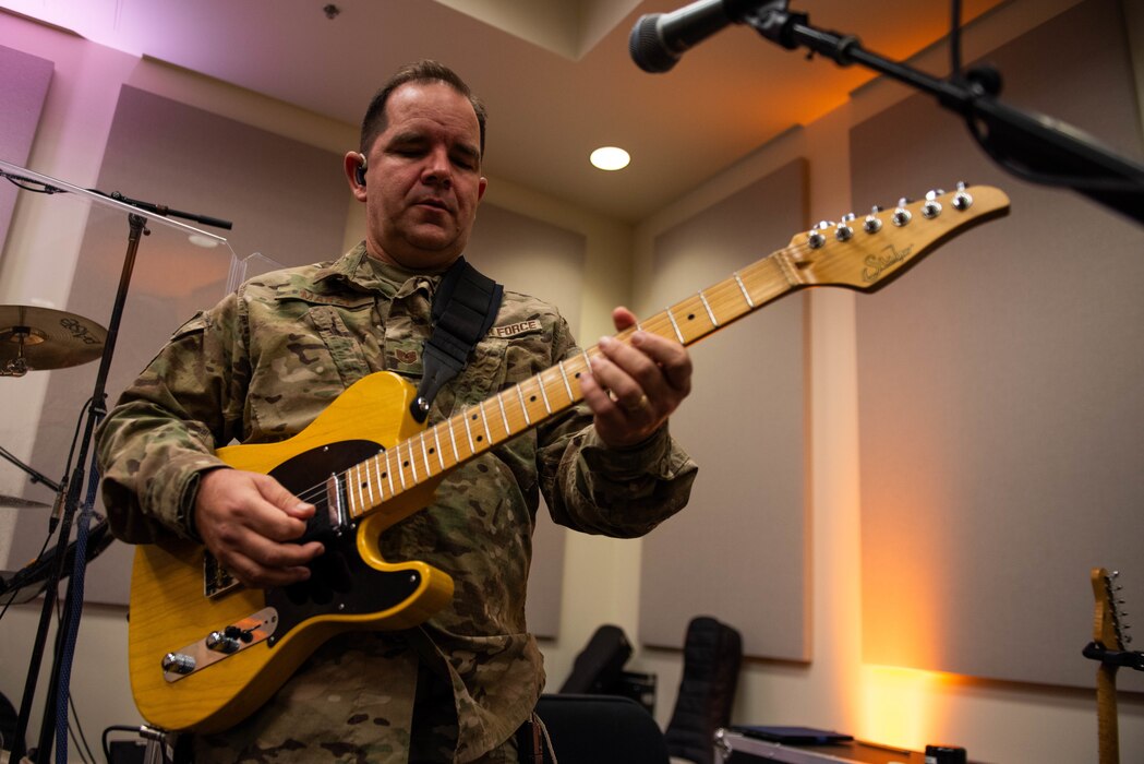 Airman plays a guitar during a rehearsal.