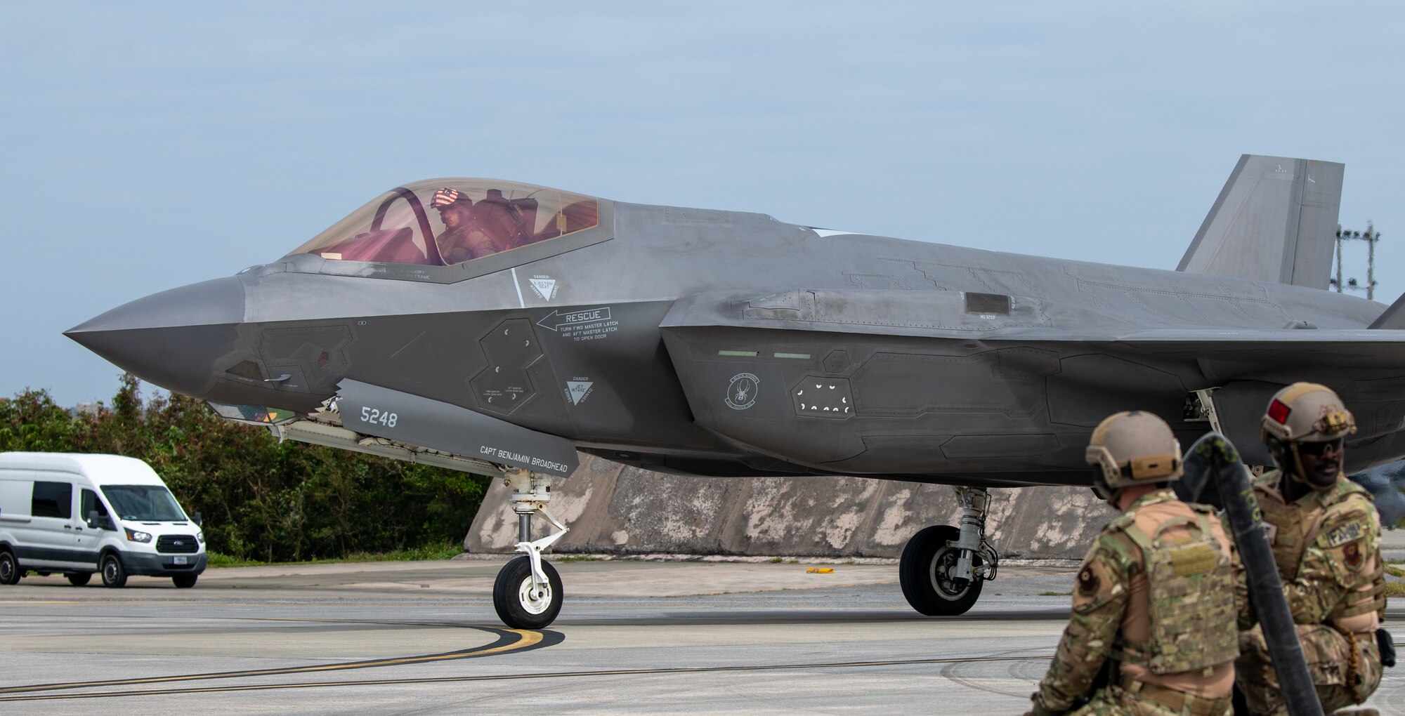 A fighter jet taxis while two Airmen standby to refuel.