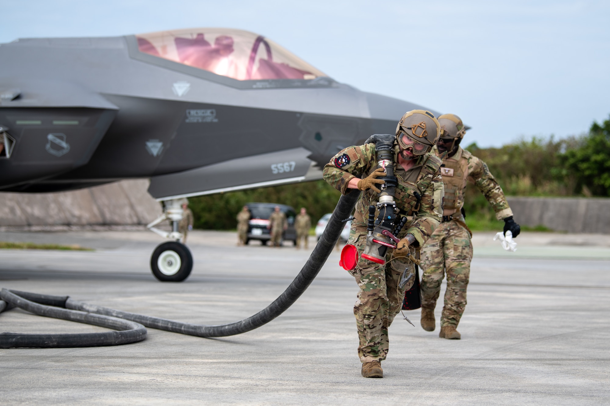 Two Airmen move a hose away from a fighter jet.