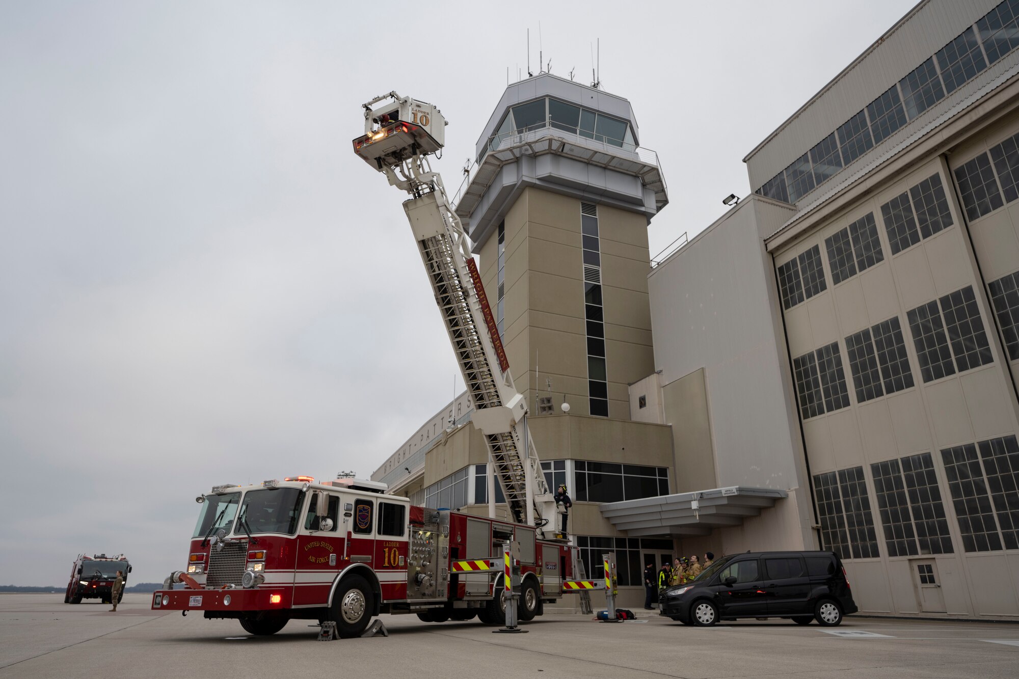 A red firetruck ladder extends over 100 feet to the top of an air traffic control tower.