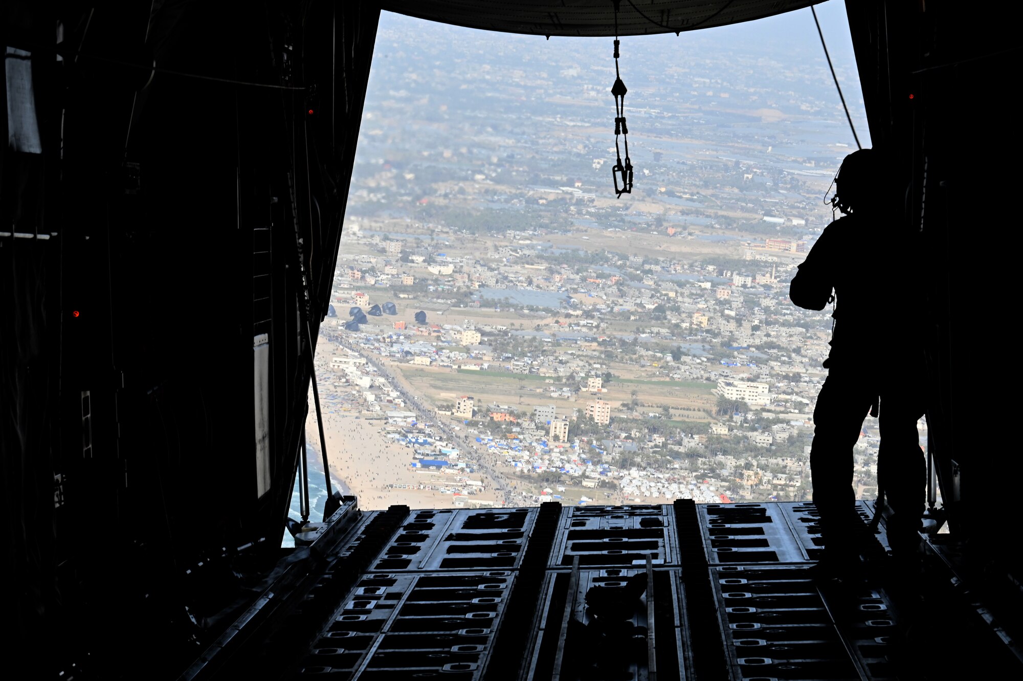 A loadmaster releases humanitarian aid pallets of packaged food over Gaza.
