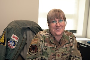 A woman in a U.S. Air Force uniform smiles while posing for a portrait indoors. She appears to be sitting and the photo is cropped from the mid-waist up.