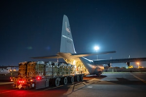 Humanitarian aid pallets rigged with parachutes for airdrop aboard a C-130J Super Hercules are prepared for takeoff .