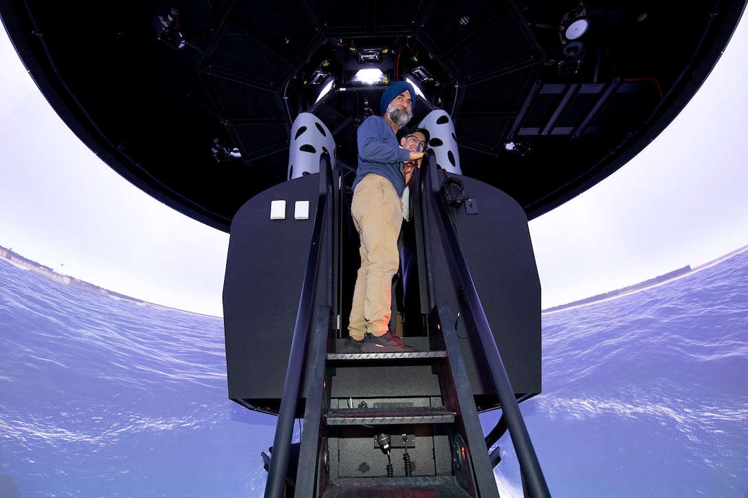 A civilian stands on a lift ladder of  a submarine simulator.
