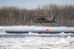 A North Dakota National Guard UH-60 Black Hawk helicopter fills up a bucket with 660 gallons of water to drop on an ice jam on the Missouri River in Bismarck, North Dakota, Feb. 29, 2024, to break up the ice and prevent flooding. Two Black Hawks dropped over 70,000 gallons of water in four hours.