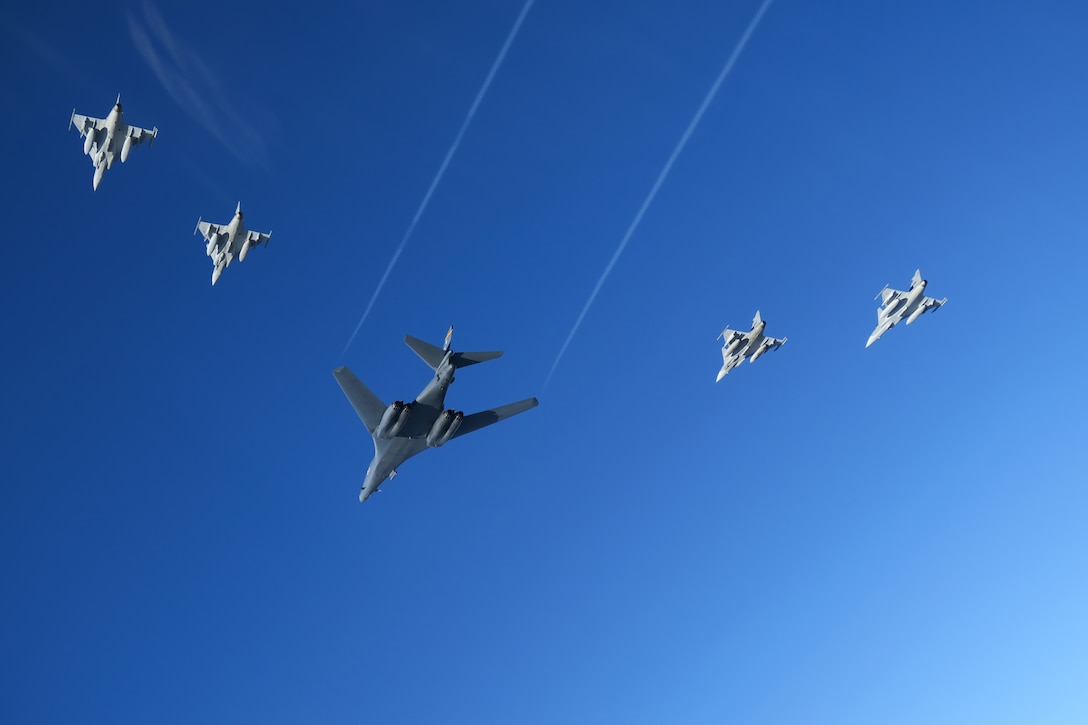 Five military aircraft fly in formation against a blue sky.