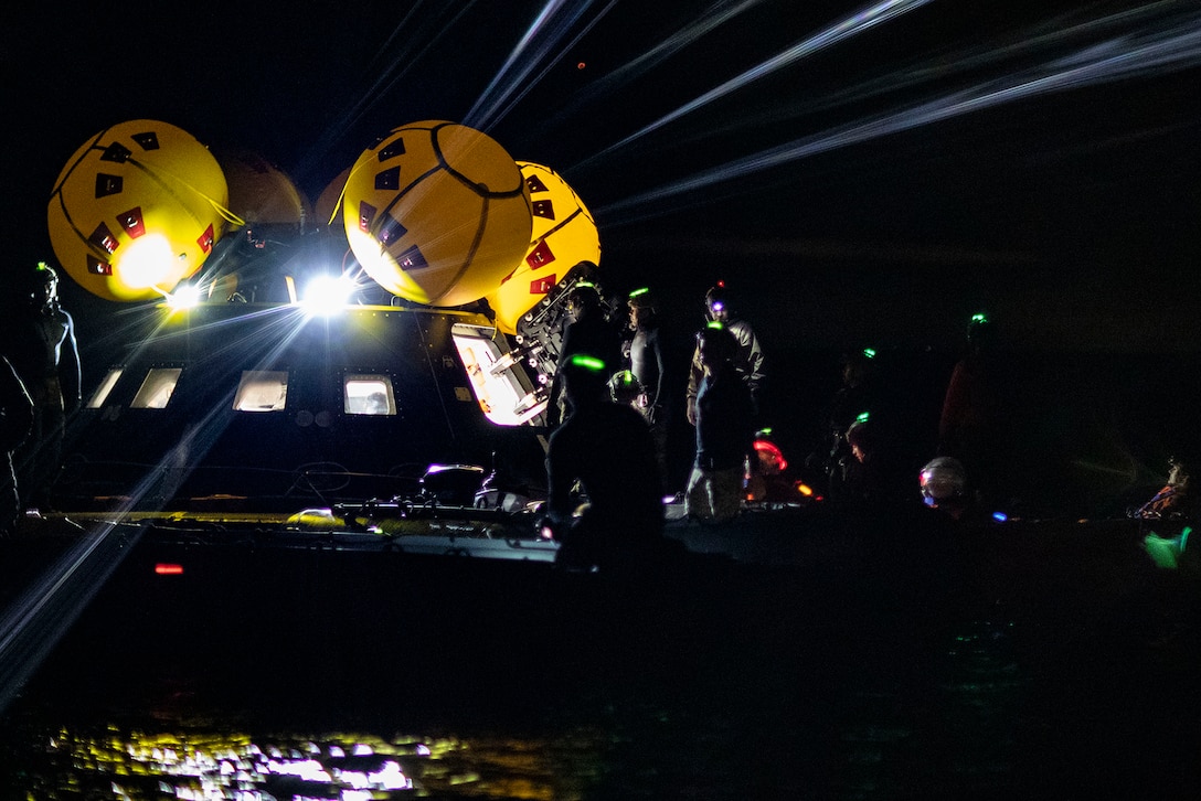 Sailors look inside a NASA crew test module at night.