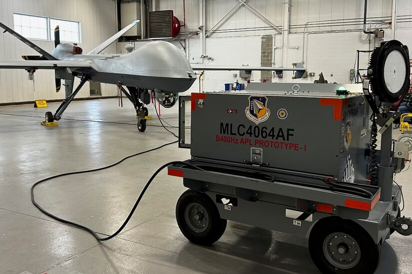 A 400 Hz Aircraft Power Lightcart is attached to an MQ-9 unmanned aerial vehicle in a hangar bay.