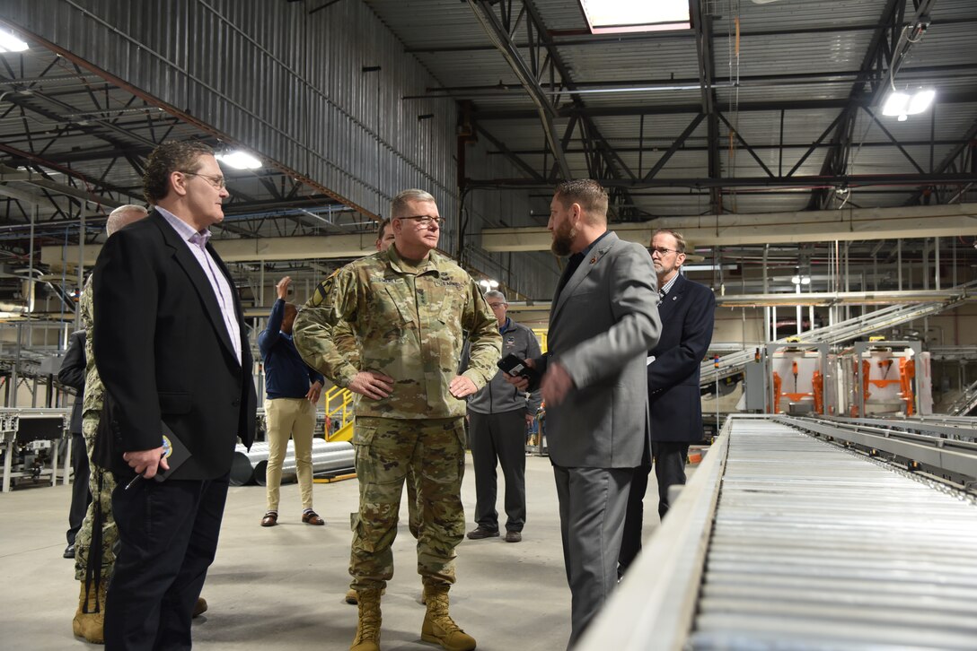 Military and civilian people in a warehouse.