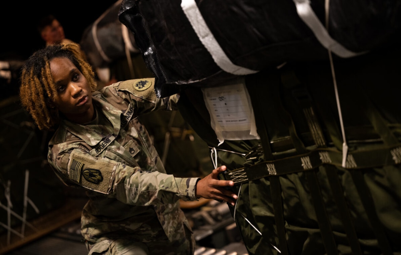 A service member in uniform pushes cargo onboard a military cargo plane.