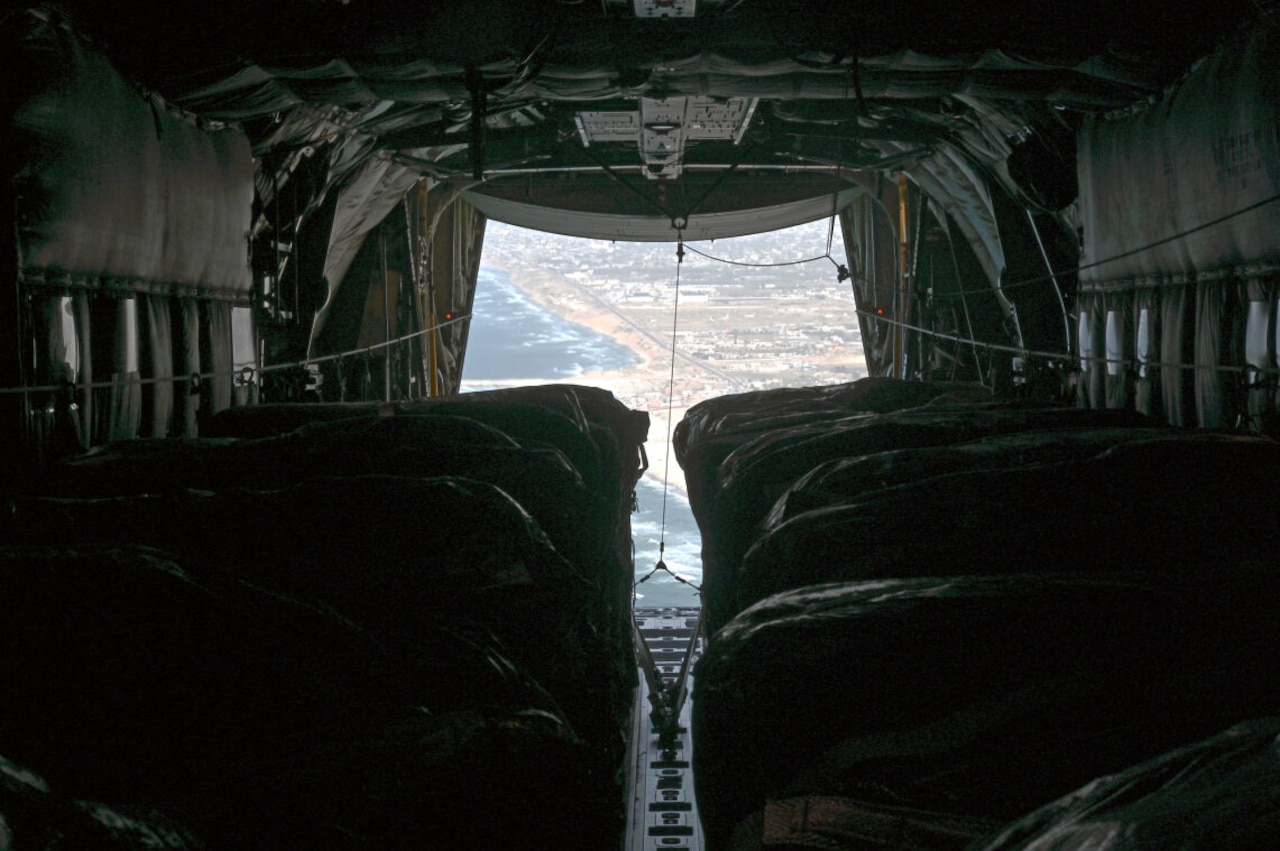 A military aircraft carrying humanitarian assistance flies with its ramp down.