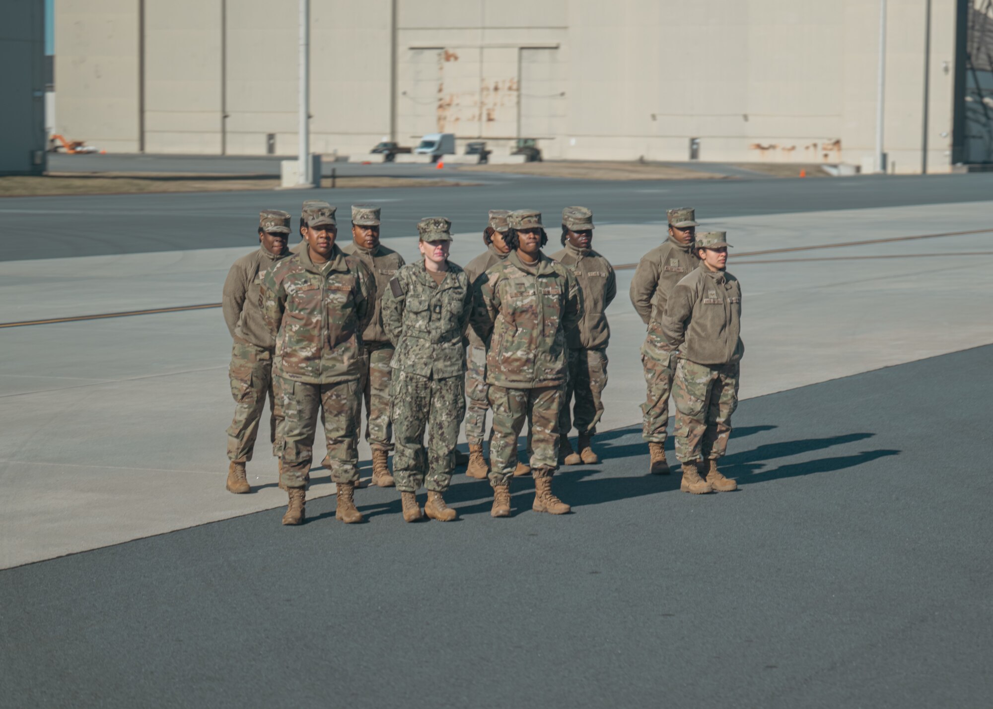 A group of female service members stand at parade rest on a flightline.
