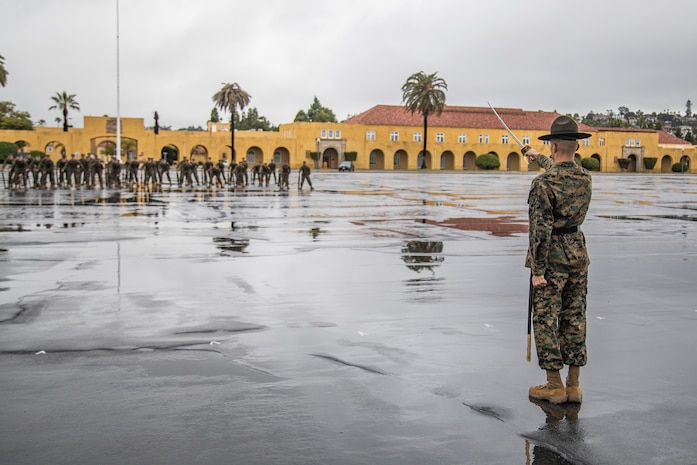 U.S. Marine Corps Staff Sgt. Rudy Dominguez Jr., a drill instructor with Mike Company, 3rd Recruit Training Battalion, calls for his platoon to form for the final drill evaluation at Marine Corps Recruit Depot San Diego, California, Mar. 2, 2024. During the final drill evaluation, the platoons are scored based on their uniforms, bearing, and movements, as well as the senior drill instructor’s cadence, sword control, and movement commands. (U.S. Marine Corps photo by Sgt. Jesse K. Carter-Powell)