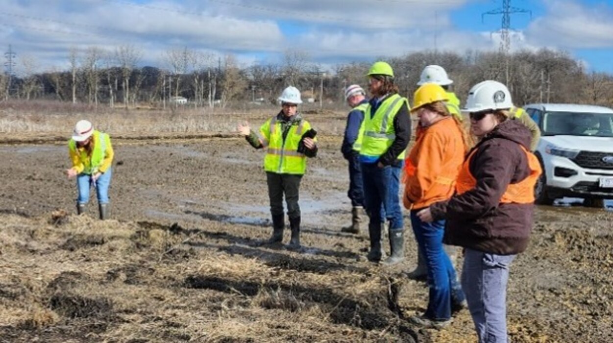 Employees in hardhats and safety vests stand on a prairie to observe the new mitigation area.